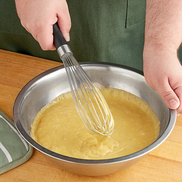An OXO Good Grips narrow piano whisk being used to mix yellow batter in a bowl.