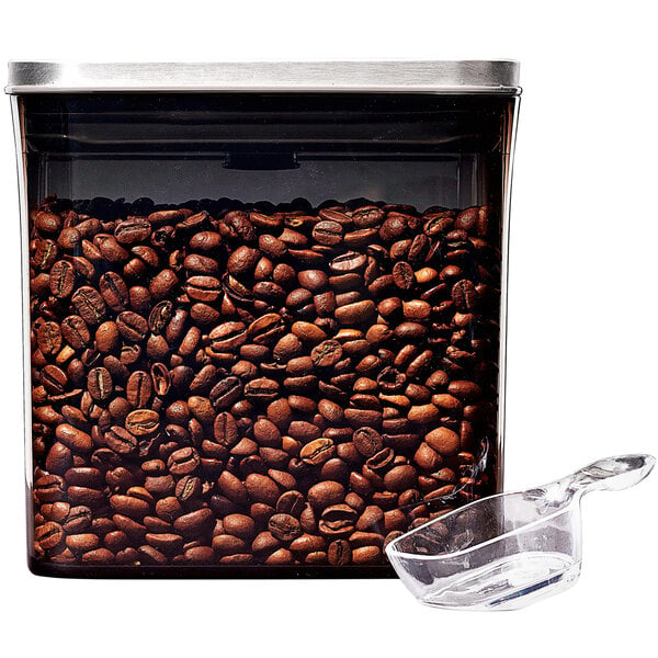An OXO clear rectangular plastic coffee container with a stainless steel POP lid and plastic scoop filled with coffee beans.
