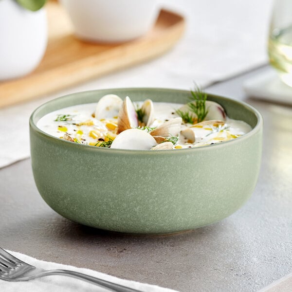 A bowl of soup with clams and herbs in a white Acopa Pangea bowl.