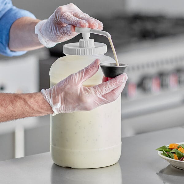 A person in gloves using a Choice condiment pump to pour liquid into a white container.