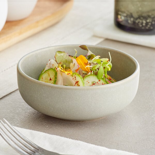 An Acopa Pangea ash matte porcelain bowl filled with salad and vegetables on a table.