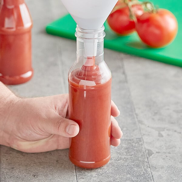 A hand pouring tomato sauce into a 12 oz. PET ring neck sauce bottle.