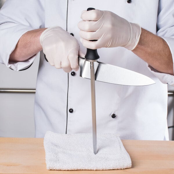 A person in white gloves using a Mercer Genesis Forged Sharpening Steel to sharpen a knife.