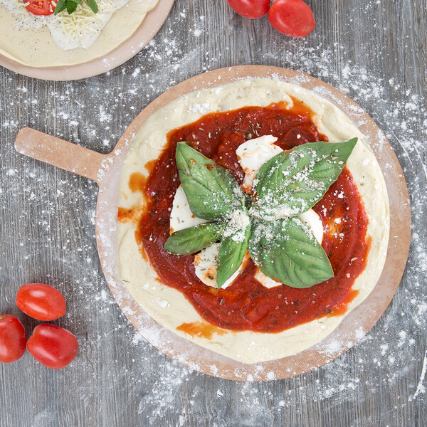 An American Metalcraft round pizza peel with a pizza topped with sauce and basil leaves.