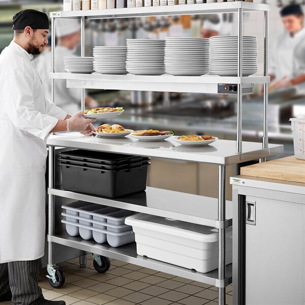 A chef using a Regency stainless steel expeditor table with double overshelf and undershelves to prepare food.