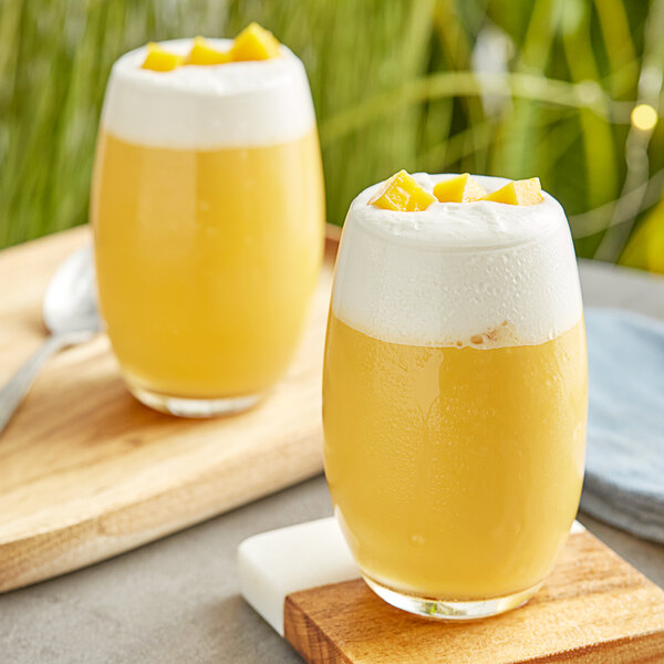 Two glasses of yellow mango juice with white foam on top.