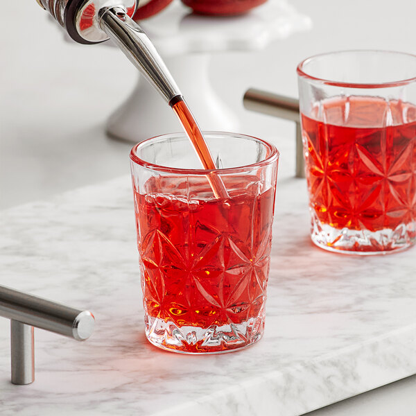 A person pouring red liquid from a pipette into an Acopa Gardenia shot glass.