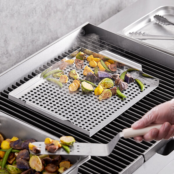 A person using a Mr. Bar-B-Q stainless steel perforated grill tray to cook vegetables on a grill.