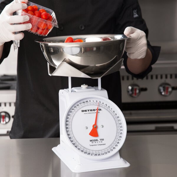 A person weighing tomatoes in a bowl on a Cardinal Detecto mechanical scale.