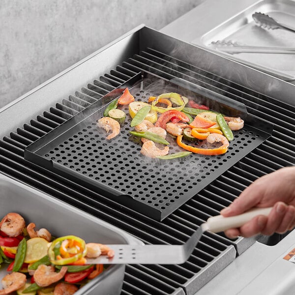 A person using a Mr. Bar-B-Q non-stick grill tray to cook shrimp and vegetables on a grill.