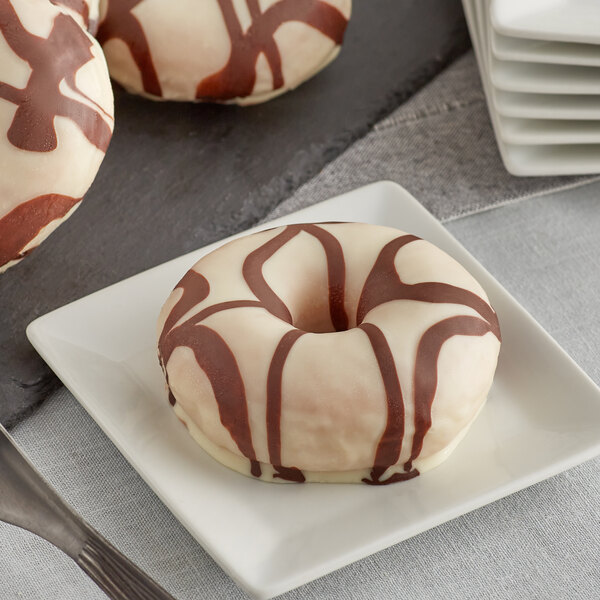 A stack of white plates with chocolate and white drizzle donuts on them.
