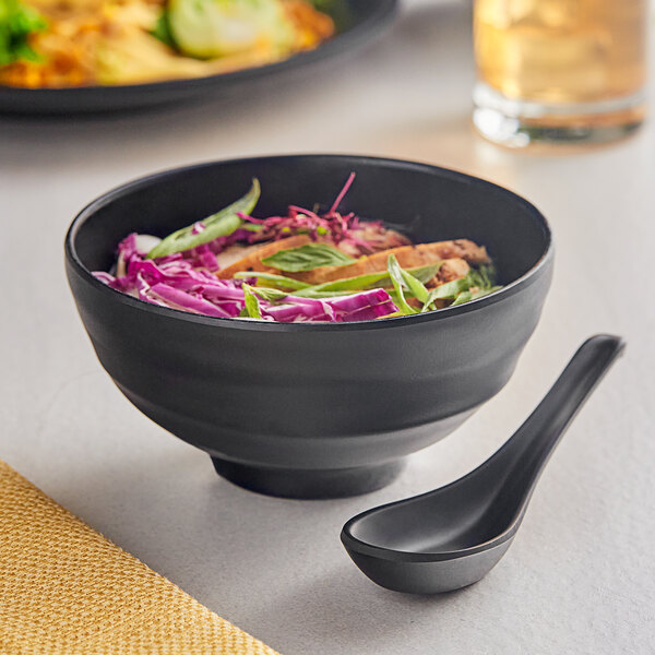 A black Acopa Izumi melamine bowl filled with food and vegetables with a spoon.