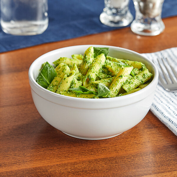 A close-up of a 15 oz. white stoneware bowl filled with pasta with pesto sauce.