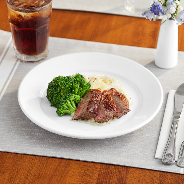 A Acopa stoneware plate with meat and broccoli on a table.