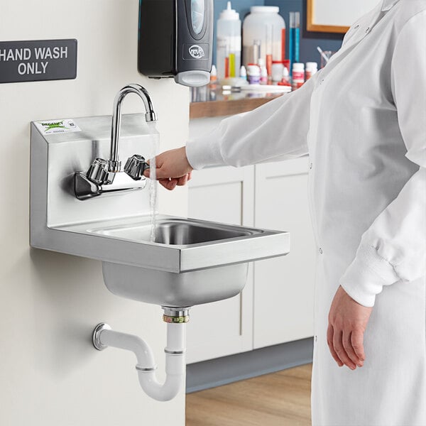 A woman in a lab coat washing her hands in a Regency wall mounted hand sink.