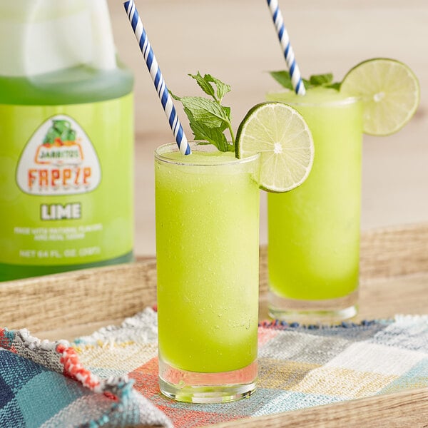A pair of green drinks in green glasses with straws and lime slices.