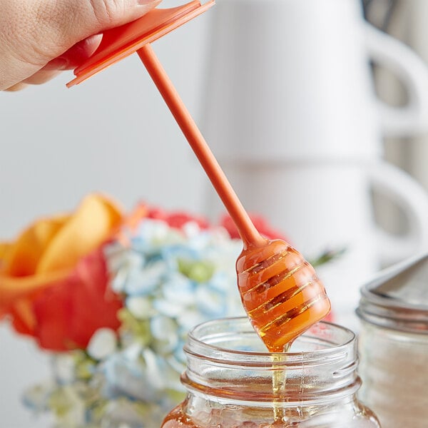 A person using a Fox Run plastic honey dipper to stir honey in a jar.