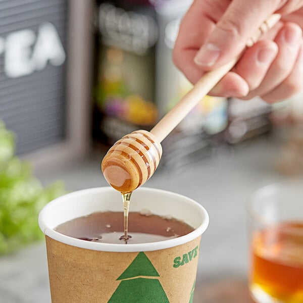 A hand holding a Fox Run wooden honey dipper over a cup of tea.