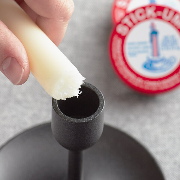 A finger using a Fox Run Stick-Um candle adhesive sticker to hold a candle stick.