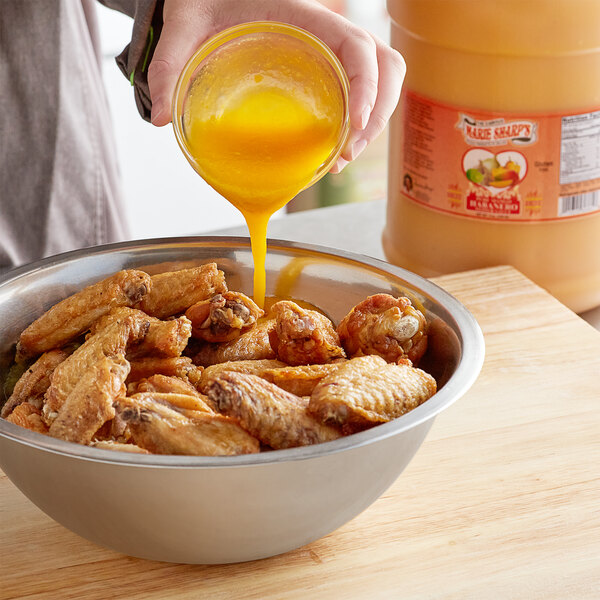 A person pouring yellow liquid from a jar into a bowl of chicken wings.