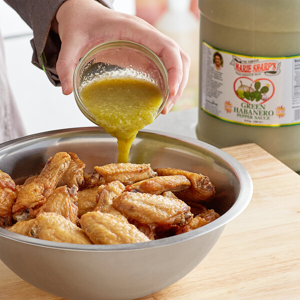 A person pouring Marie Sharp's green habanero sauce into a bowl of chicken wings.