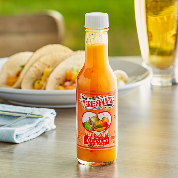 A bottle of Marie Sharp's Mango Habanero hot sauce on a table with tacos.