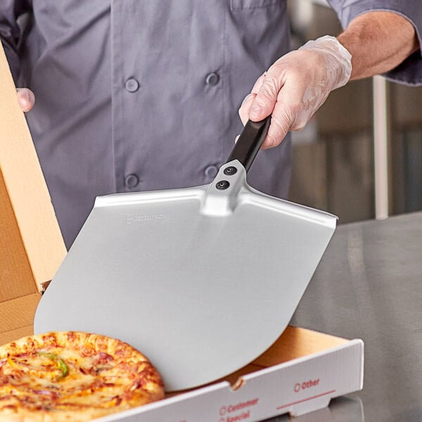A person holding a GI Metal rectangular pizza peel over a pizza.