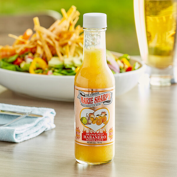 A close up of a bottle of Marie Sharp's Orange Pulp Habanero Hot Sauce next to a bowl of salad.