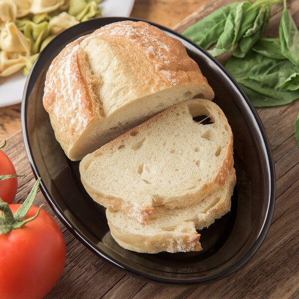 A loaf of bread on a Carlisle black oval platter with tomatoes and pasta.