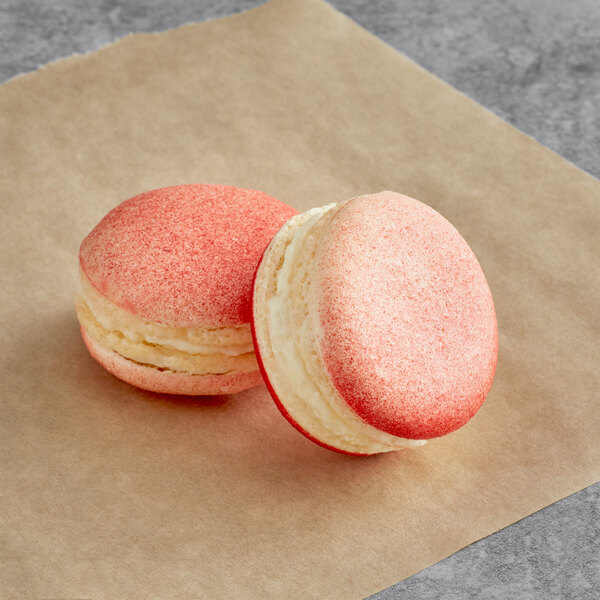 Two pink and white Macaron Centrale lychee macarons on a piece of paper.