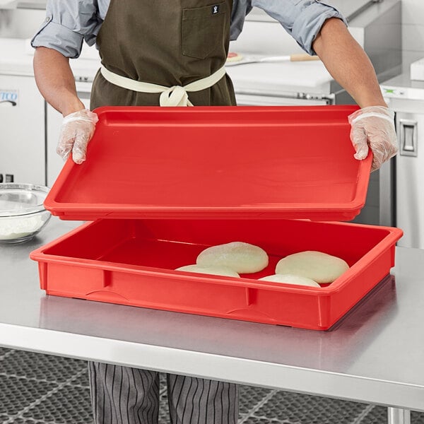 A person in a chef's uniform holding a red Baker's Mark dough proofing box lid.