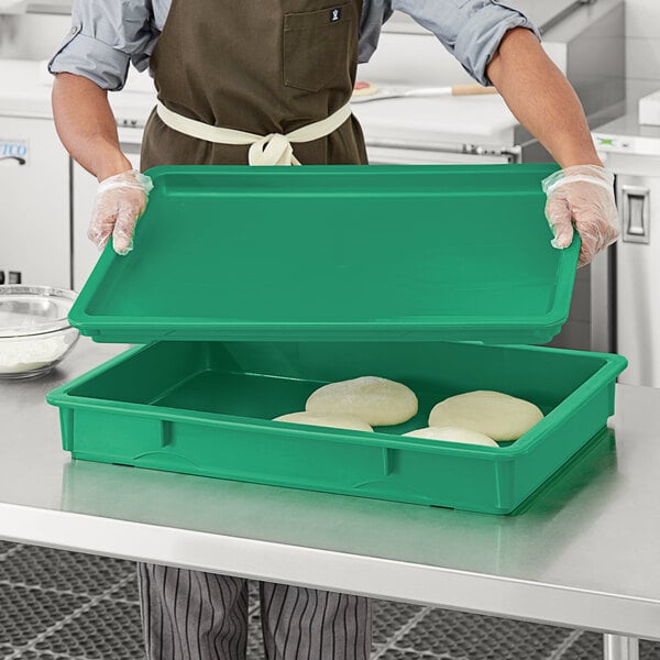 A person in a chef's uniform using a green rectangular Baker's Mark dough proofing box lid.