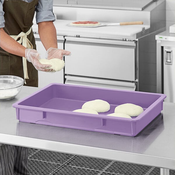 A person in a purple apron using a purple Baker's Mark dough proofing box to hold white dough.