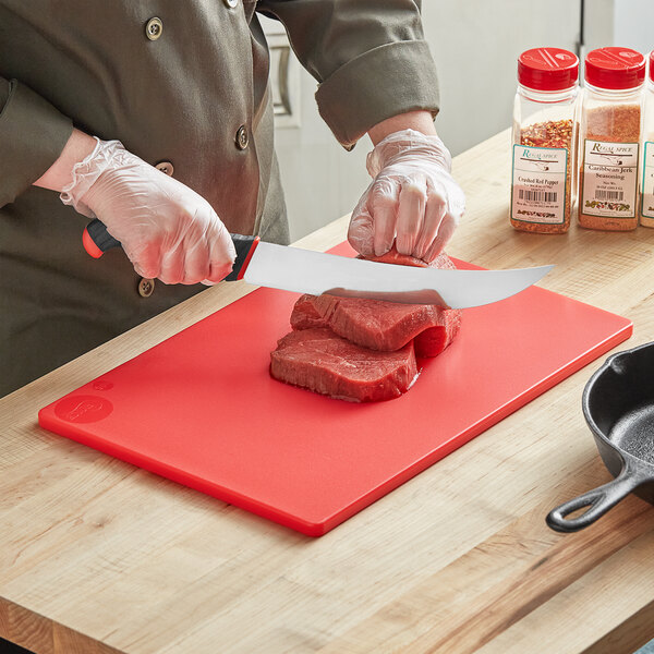 A person cutting meat on a red Choice cutting board.