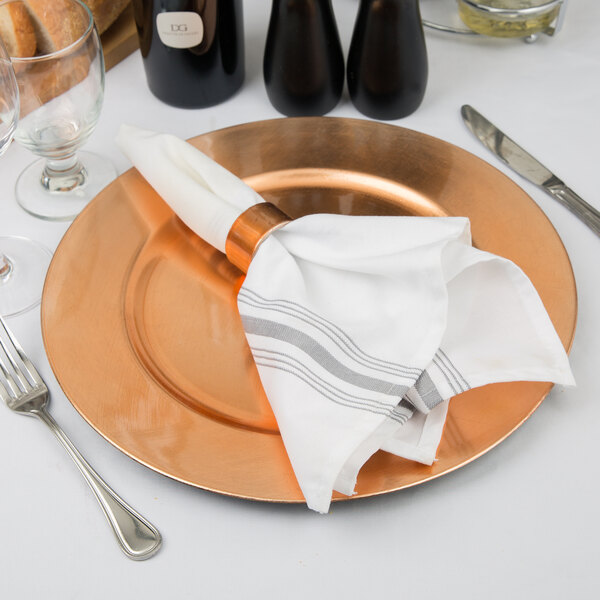 A Tabletop Classics by Walco copper charger plate with a napkin and silverware on it.