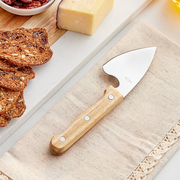 An Acopa stainless steel hard cheese cleaver with a wood handle cutting cheese on a wooden cutting board.