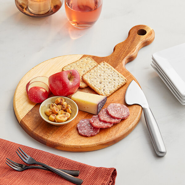 An Acacia wood board with cheese, crackers, and a knife on a table.