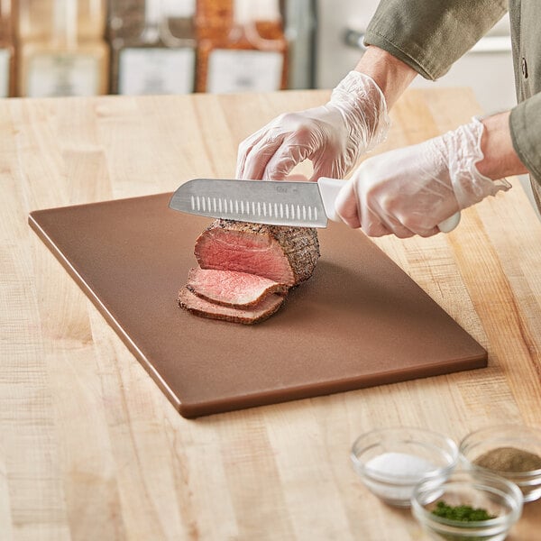 A person cutting a piece of meat on a Choice brown polyethylene cutting board.