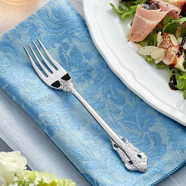 An Acopa Ophelia stainless steel salad fork on a plate with a salad on a table with a blue tablecloth.
