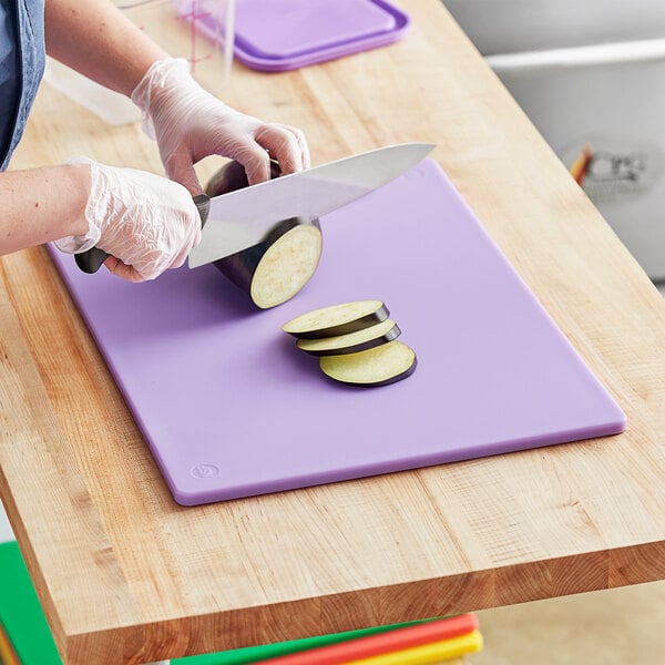 A person cutting eggplant on a purple Choice cutting board.