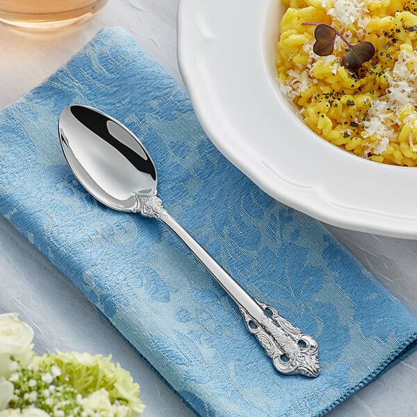 An Acopa Ophelia stainless steel dinner spoon on a blue napkin next to a bowl of food.