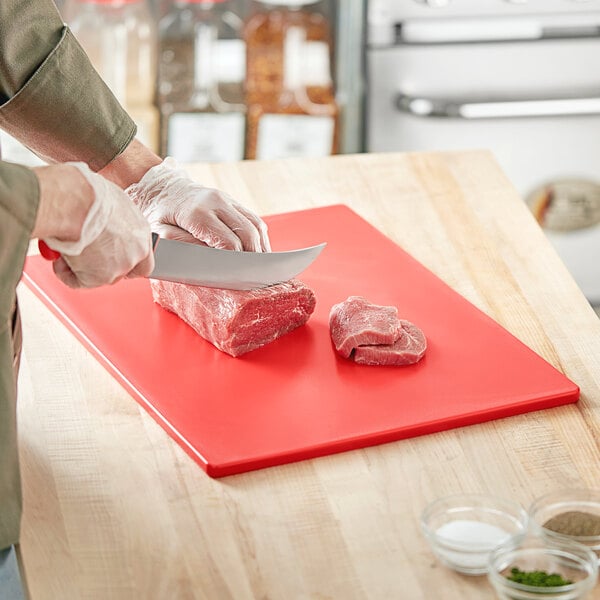 A person cutting meat on a red Choice cutting board.