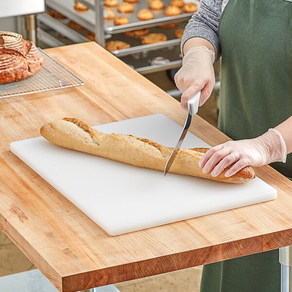 A person cutting a loaf of bread on a white polyethylene cutting board.