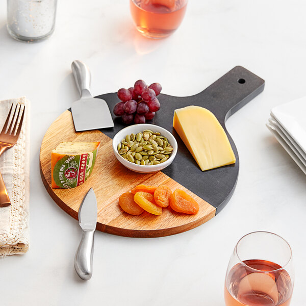 An Acopa acacia wood and slate cheese board with fruit, nuts, and dried apricots on it.