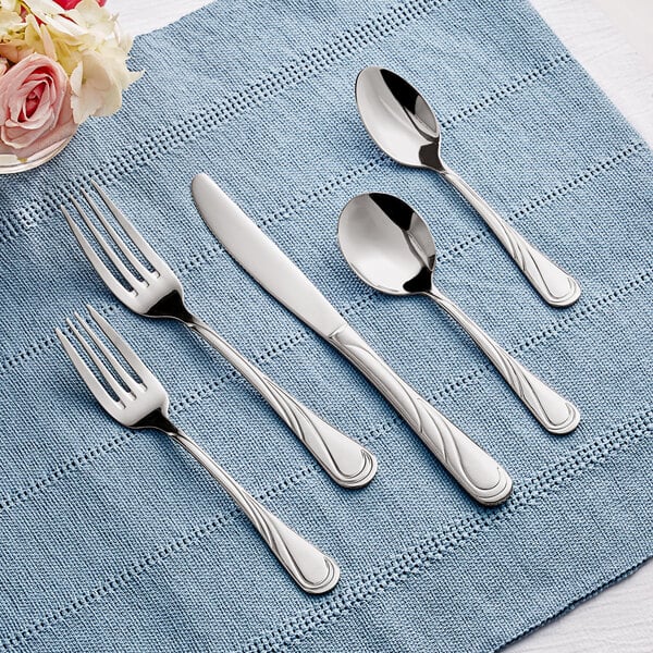 Acopa Swirl 18/8 stainless steel flatware on a blue cloth with a knife and spoon.