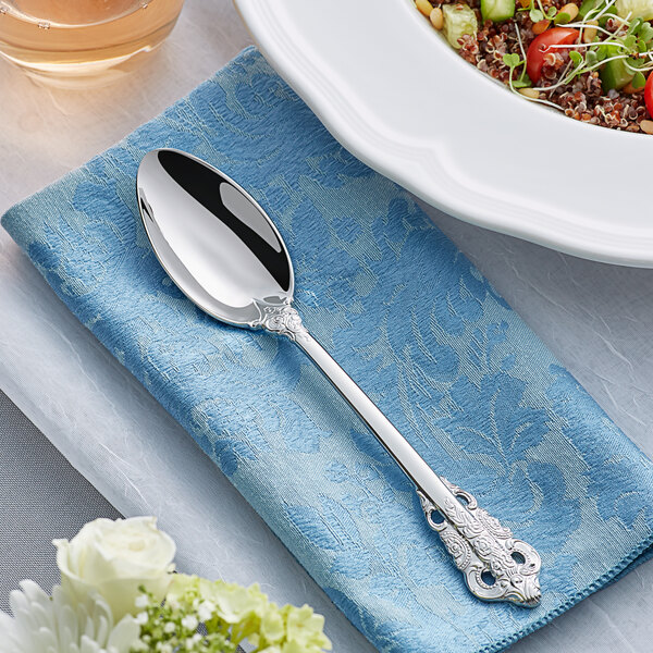 An Acopa stainless steel serving spoon on a blue napkin next to a bowl of food.