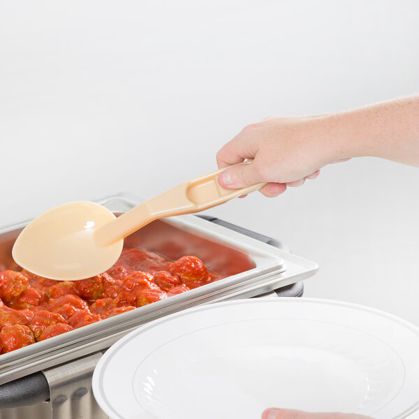 A person using a Cambro beige salad bar spoon to put food in a bowl.