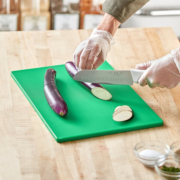 A person cutting eggplant on a green Choice cutting board.