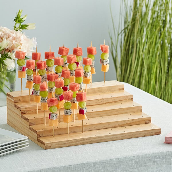An Acopa natural wood skewer holder with fruit on it.