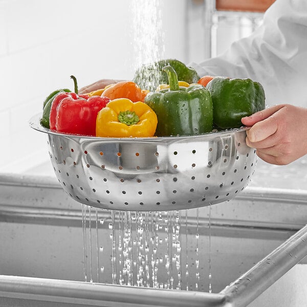 A person washing green and yellow bell peppers in a stainless steel colander.